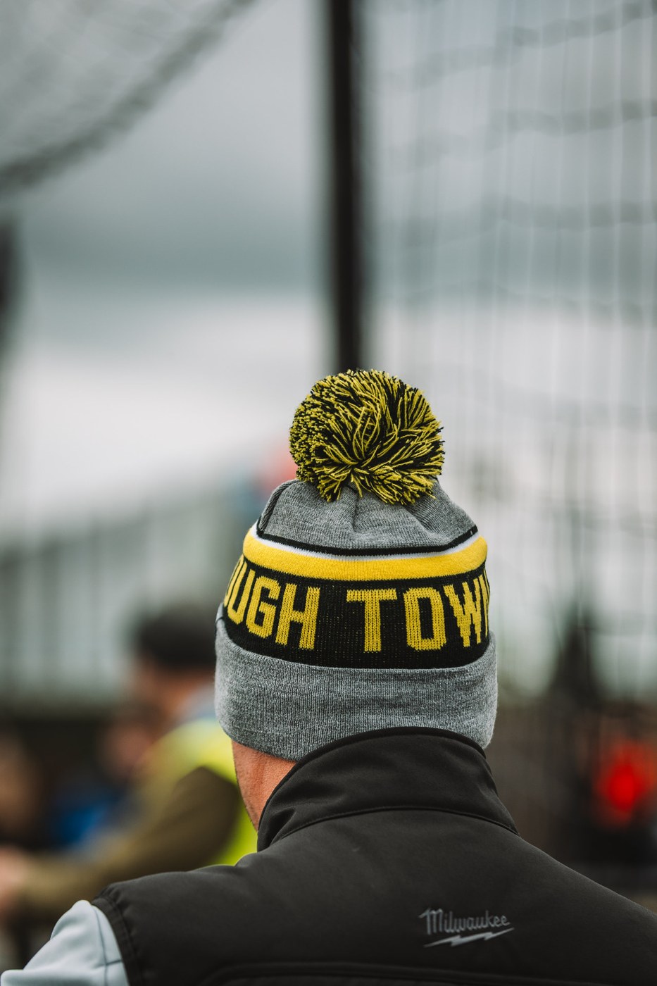 Supporter wearing a yellow, black and grey Harborough Town bobble hat