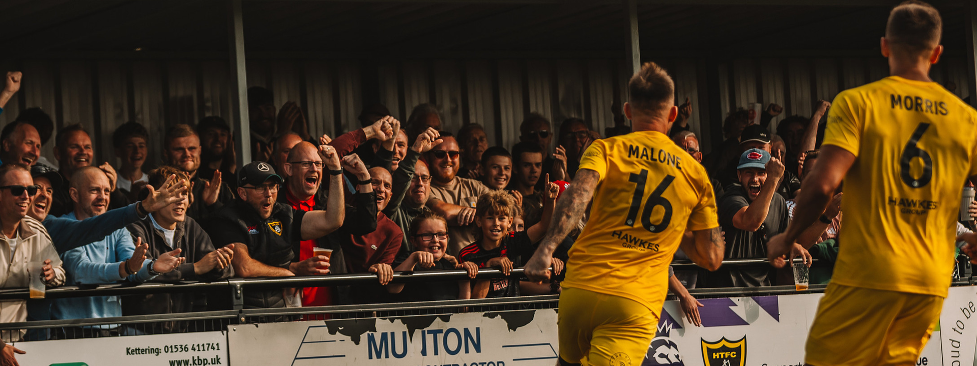 Harborough Town players in yellow shirts greeting supporters beside the pitch at Harborough Town Community Football Ground